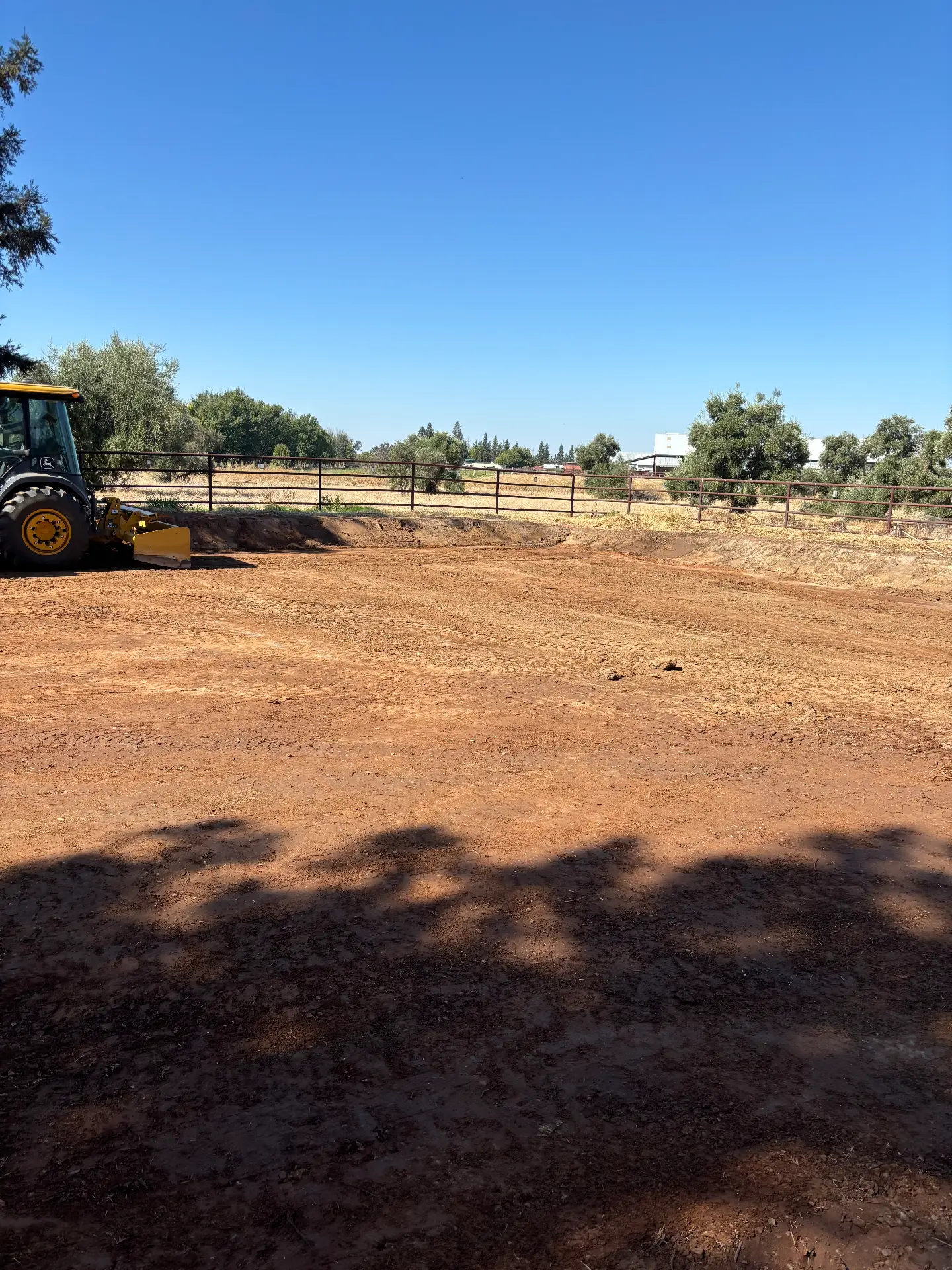 Graded dirt area beside a fence with a tractor