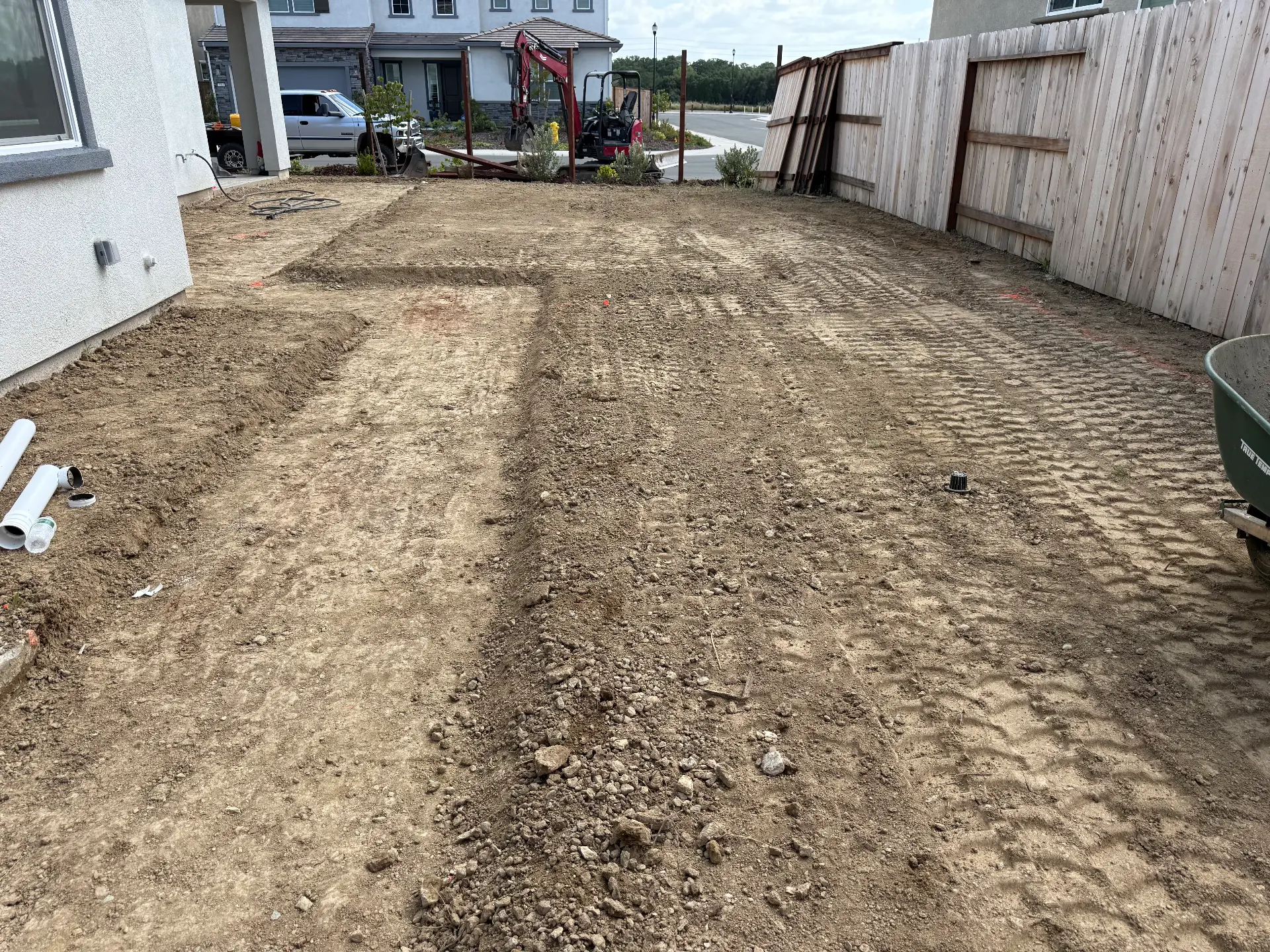 Graded residential yard with machine tracks and compact excavator
